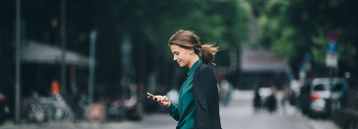 Business woman walking in the city. She's checking her mobile phone. 
