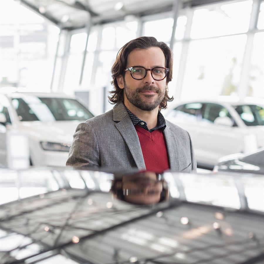 Man is standing next to a new car at a car dealer's. 