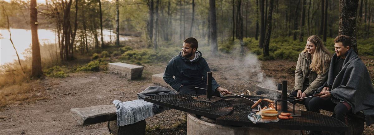 Vandrare i skogen som tar en paus framför öppen eld vid vattnet