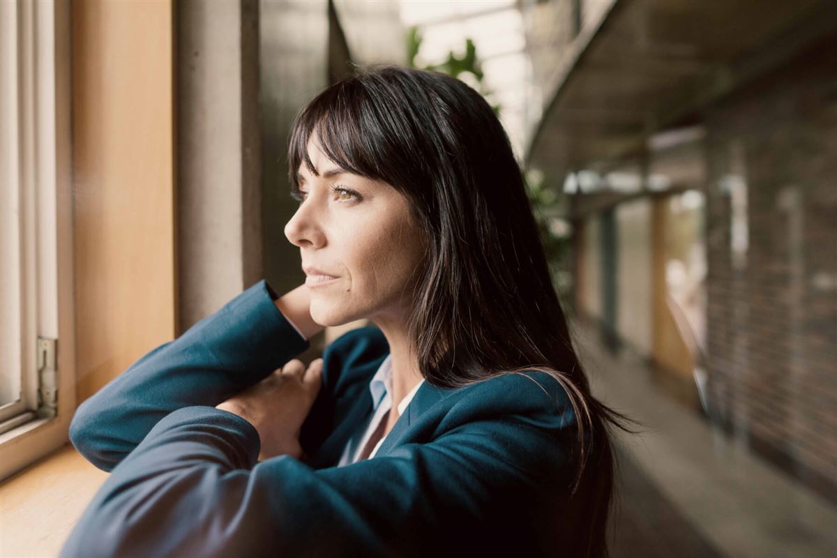 A woman dressed in a business outfit is looking out the window in an office building. 