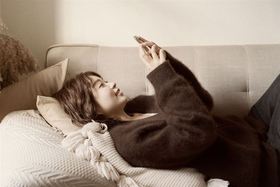 A woman is lying on the couch. She is in the process of starting saving using the mobile app.