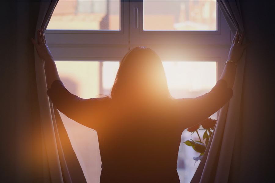 Woman opening curtains to let the sun in.